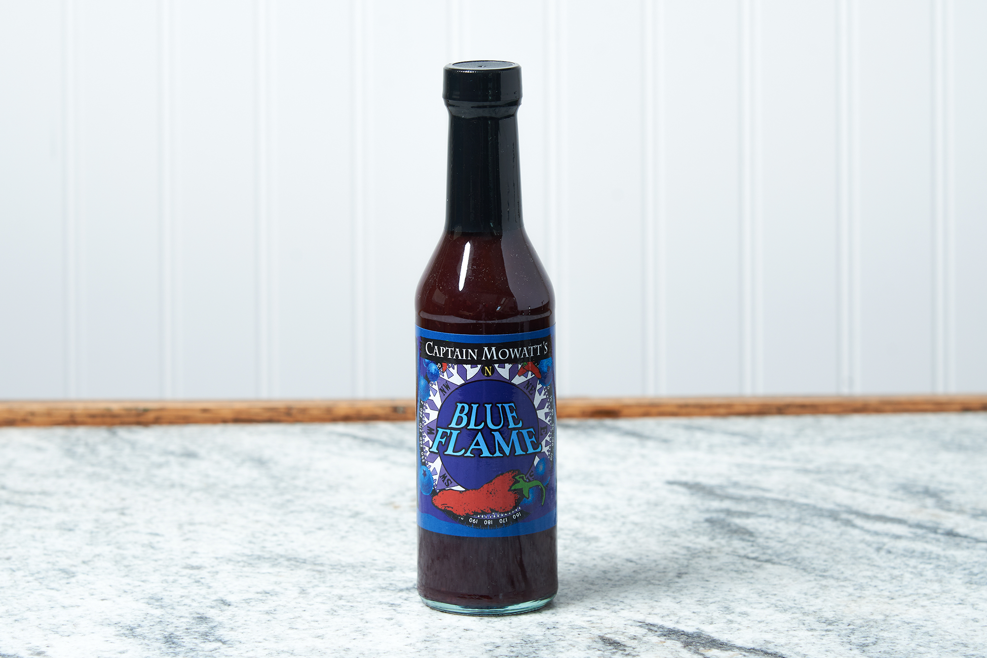 A bottle of Captain Mowatt's Blue Flame Sauce sits on a marble countertop.