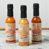 An assortment of Chad's Hot Sauce sits on a marble countertop. The flavors include: Single Reef, Double Reef, and Code Zero - No Heat.