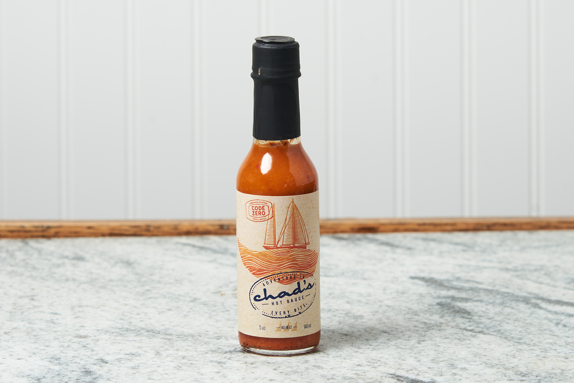 A bottle of Chad's Code Zero - No Heat Hot Sauce sits on a marble countertop.