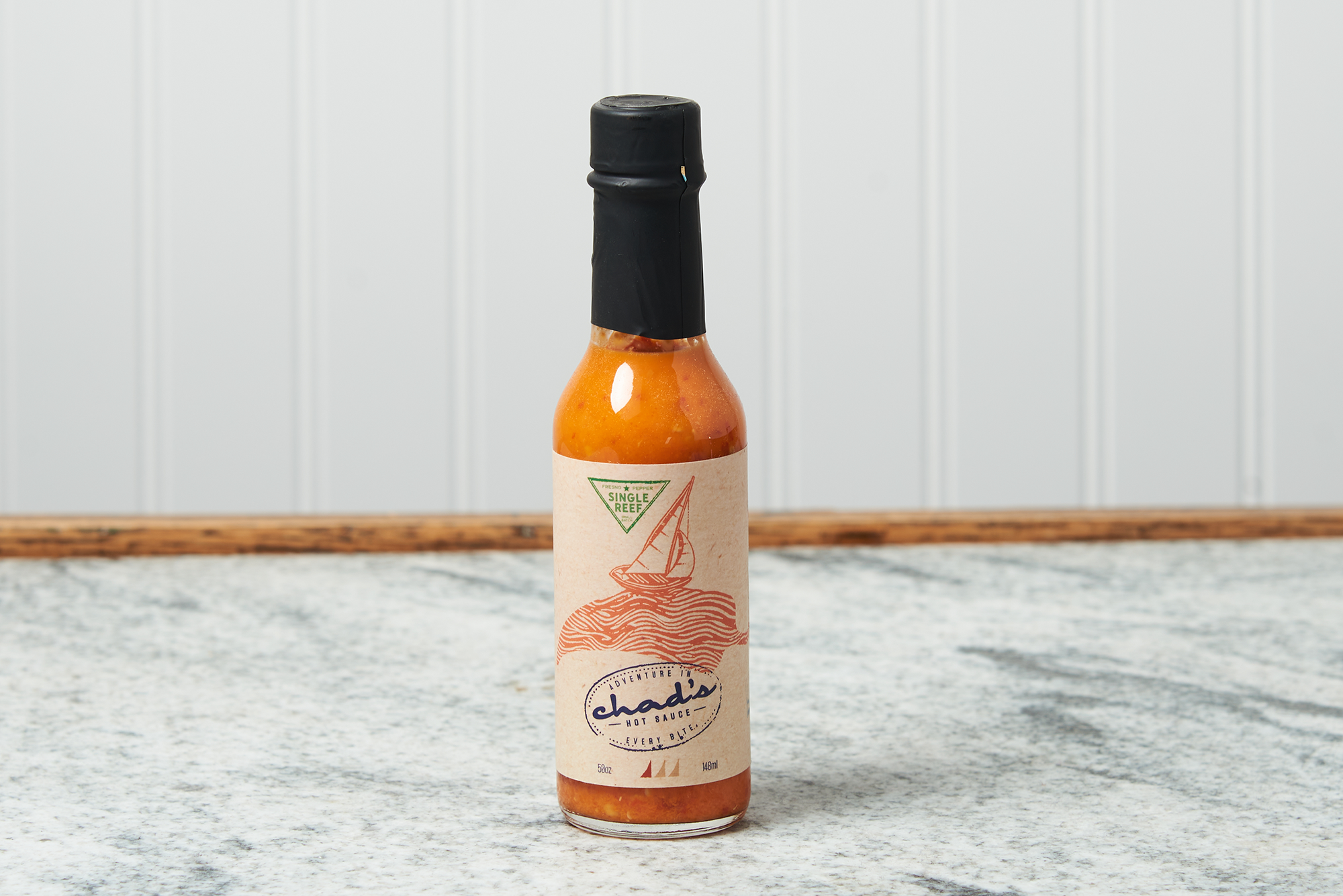 A bottle of Chad's Single Reef Hot Sauce sits on a marble countertop.