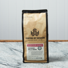 A bag of Coffee By Design Espresso Bella Crema coffee sits on a marble countertop.