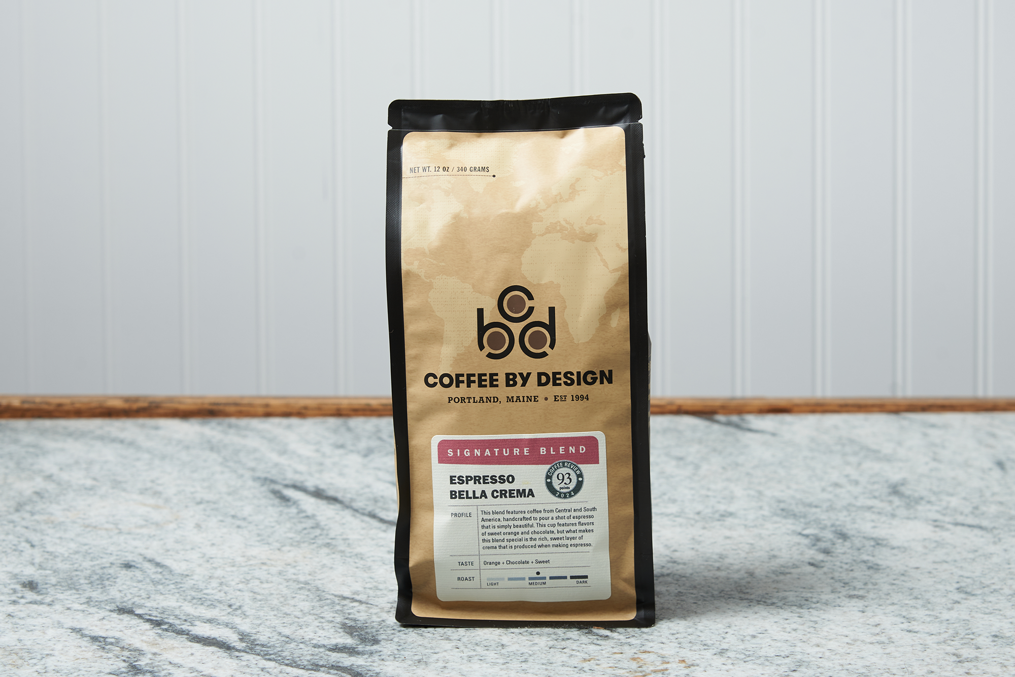 A bag of Coffee By Design Espresso Bella Crema coffee sits on a marble countertop.