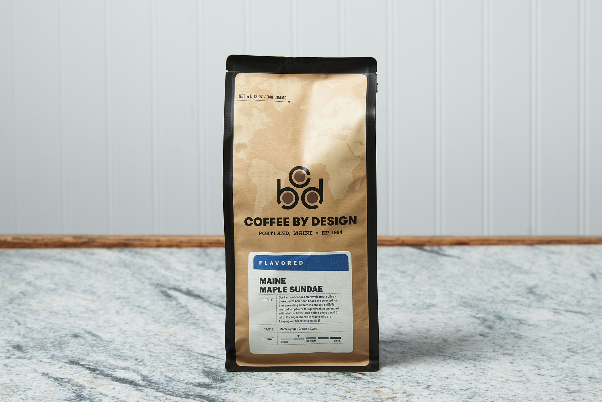A bag of Coffee By Design Maine Maple Sundae coffee sits on a marble countertop.