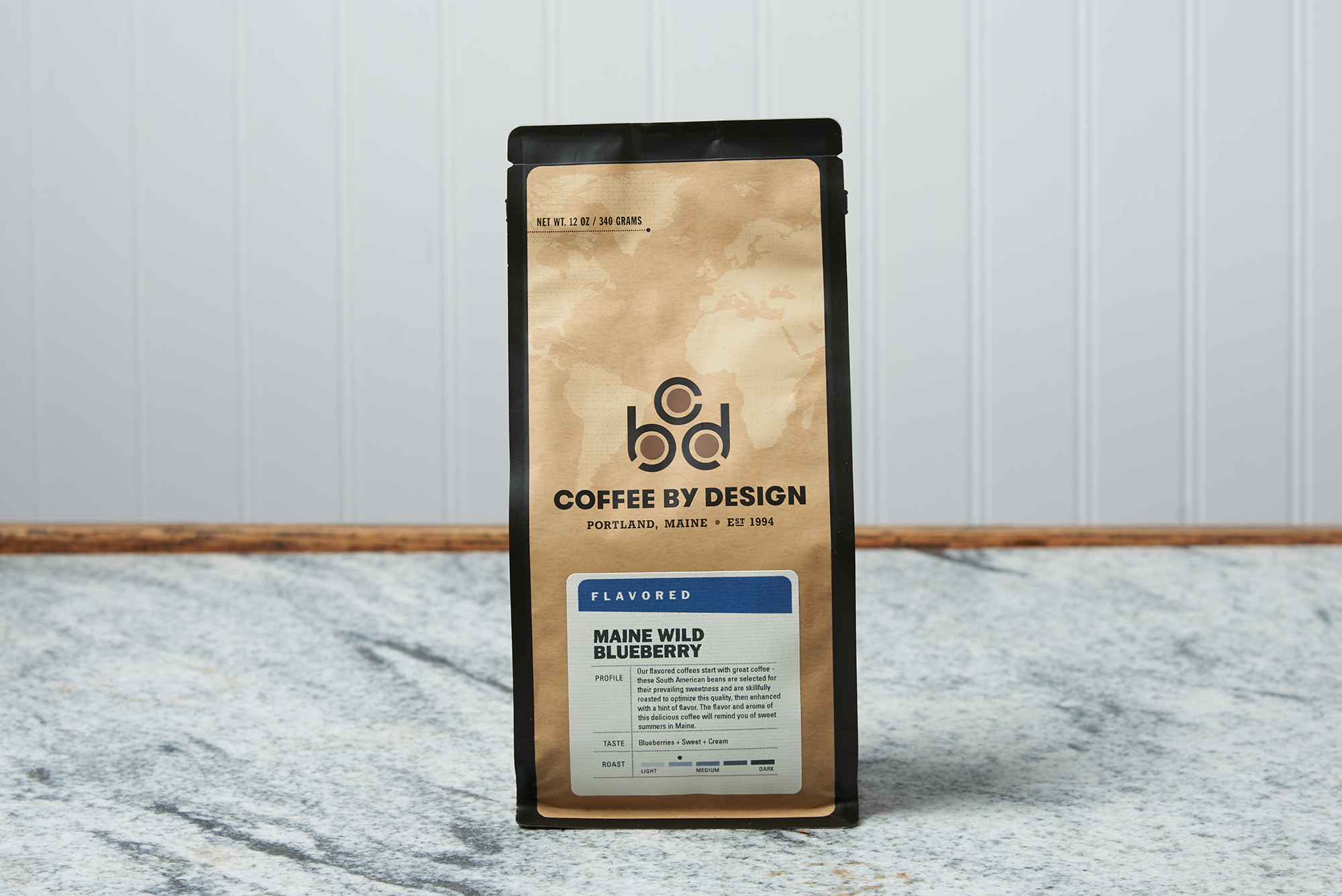A bag of Coffee By Design Maine Wild Blueberry coffee sits on a marble countertop.