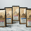 Five bags of Coffee By Design coffee sit on a marble countertop.