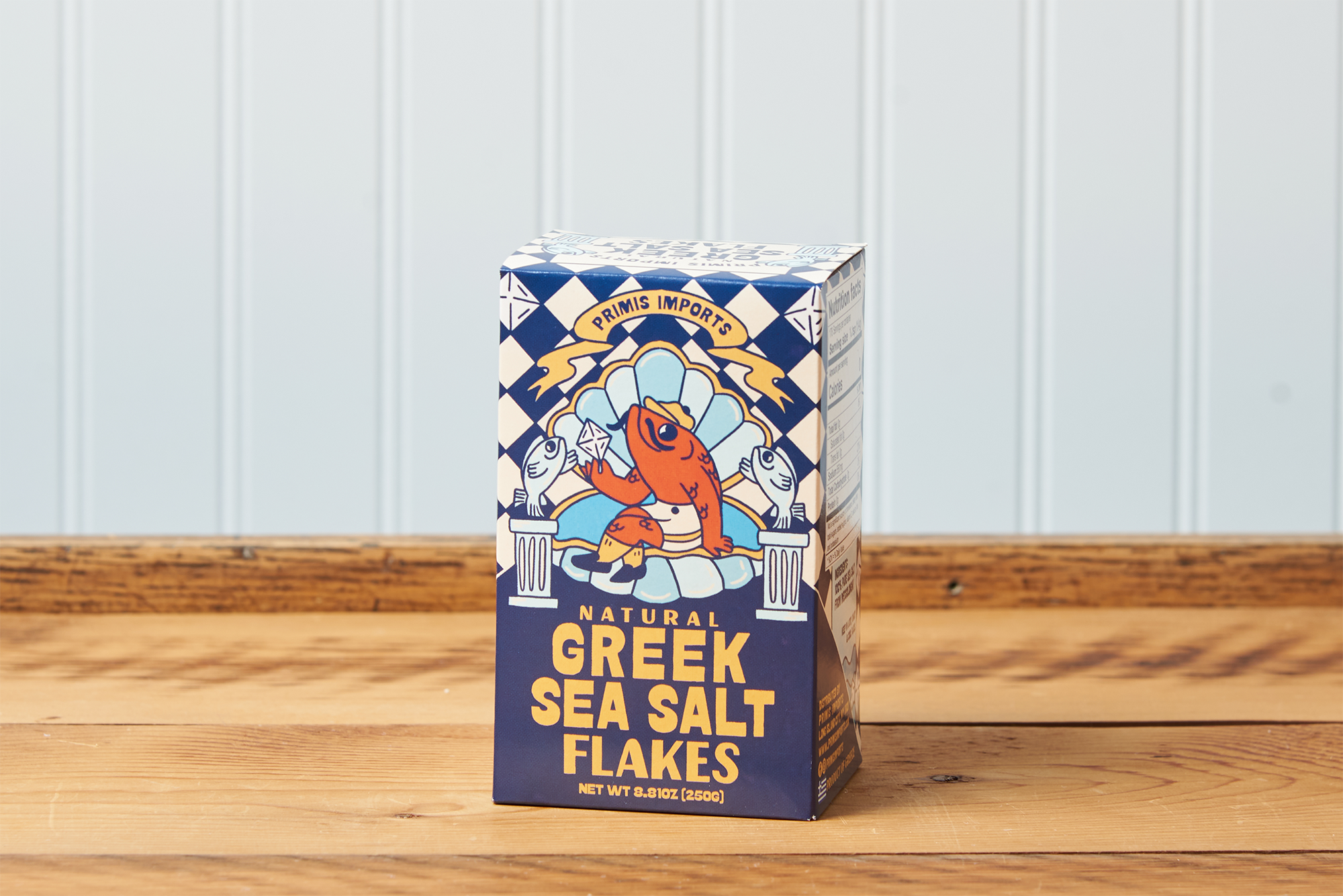 A front-facing view of a box of Greek Sea Salt Flakes sitting on a wooden table.
