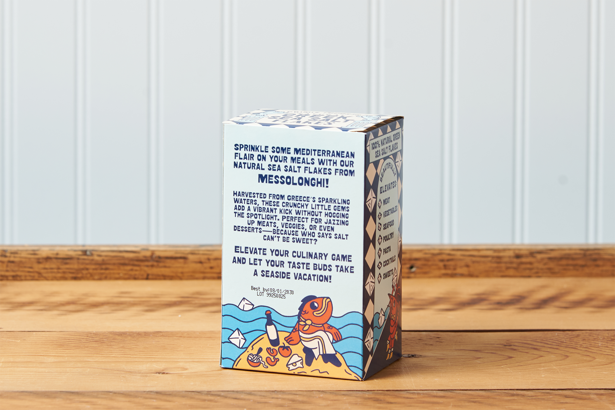 A rear-facing view of a box of Greek Sea Salt Flakes sitting on a wooden table.