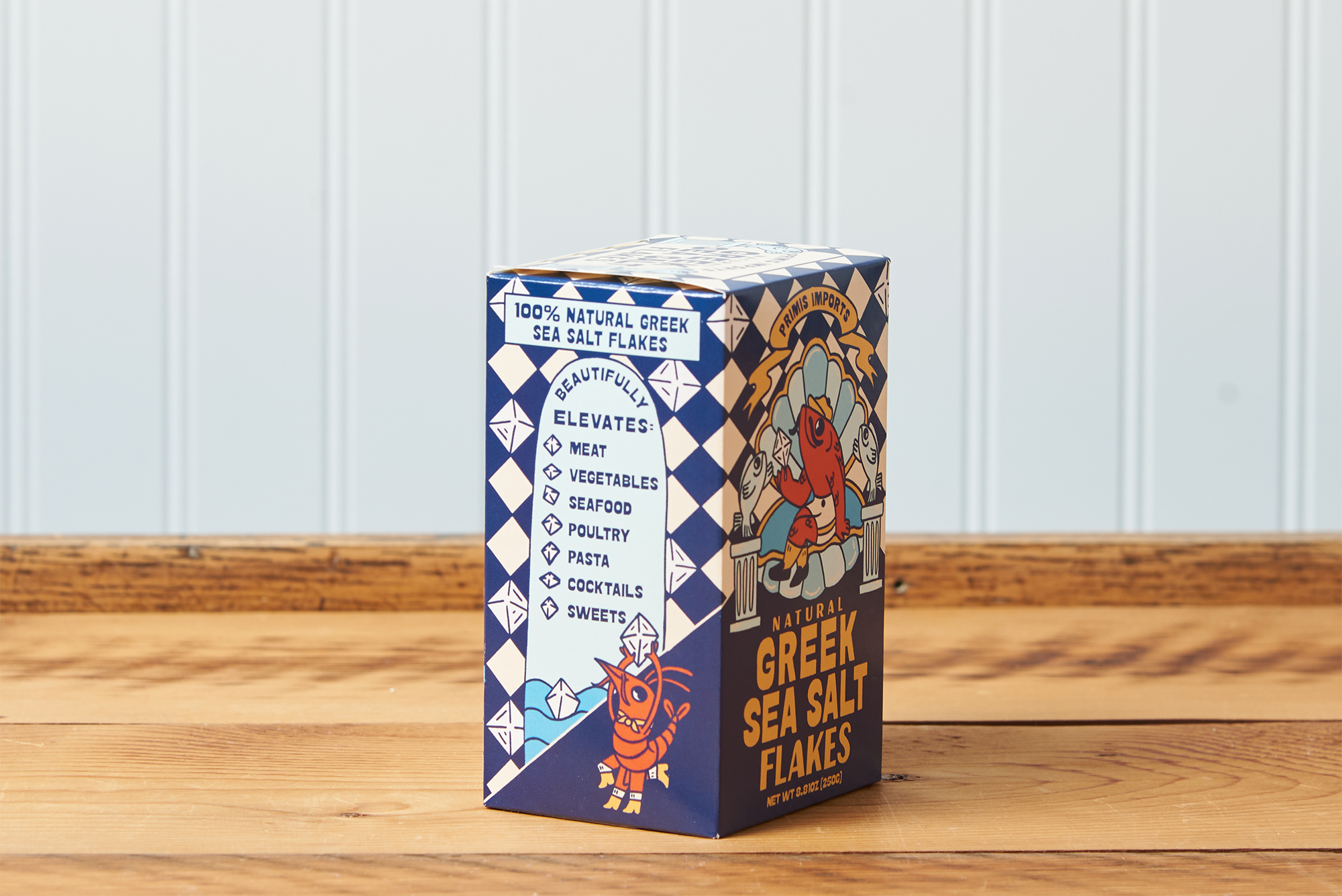 A side-facing view of a box of Greek Sea Salt Flakes sitting on a wooden table.
