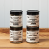 Five jars of Gryffon Ridge spices sit on a wooden tabletop. The spices include Saigon Cinnamon Powder, Coriander Seed Ground, Whole Nutmeg, and Fennel Seed.