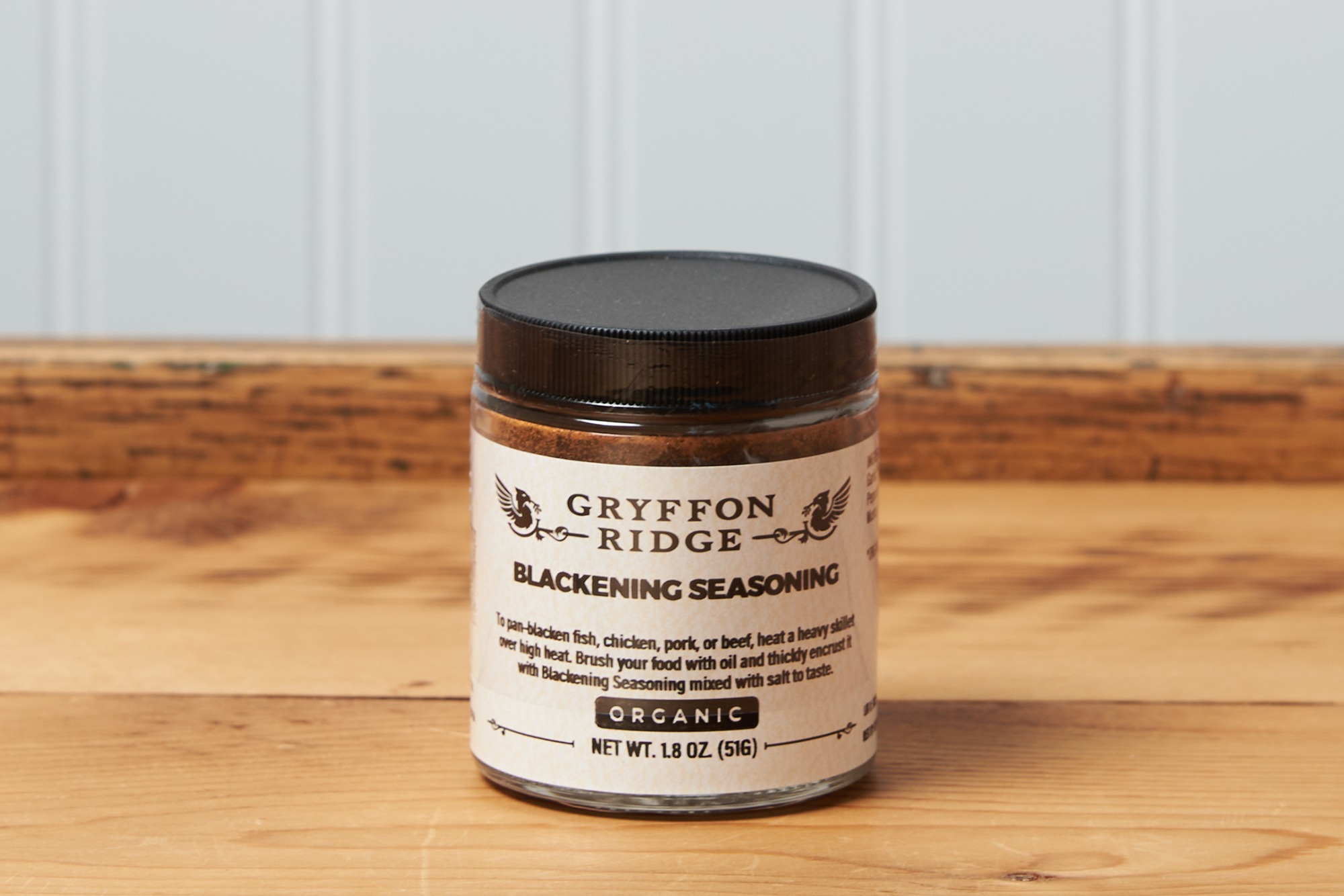 A jar of Gryffon Ridge Blackening Seasoning sits on a wooden tabletop.