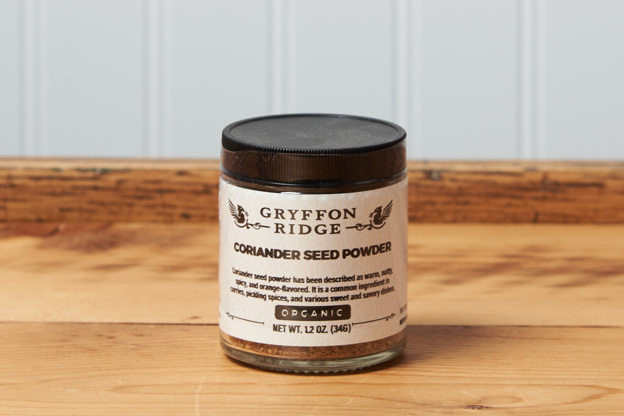 A jar of Gryffon Ridge Coriander Seed Powder sits on a wooden tabletop.