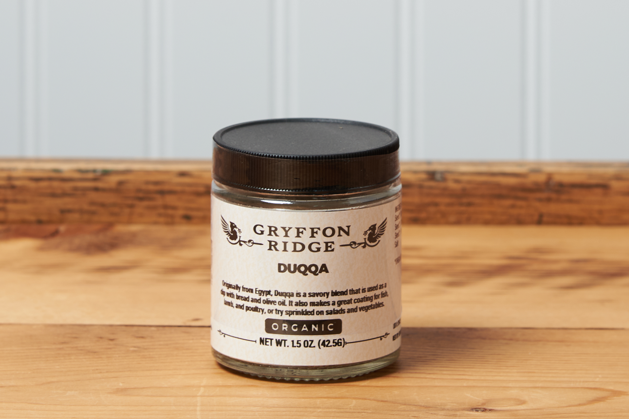 A jar of Gryffon Ridge Duqqa sits on a wooden tabletop.
