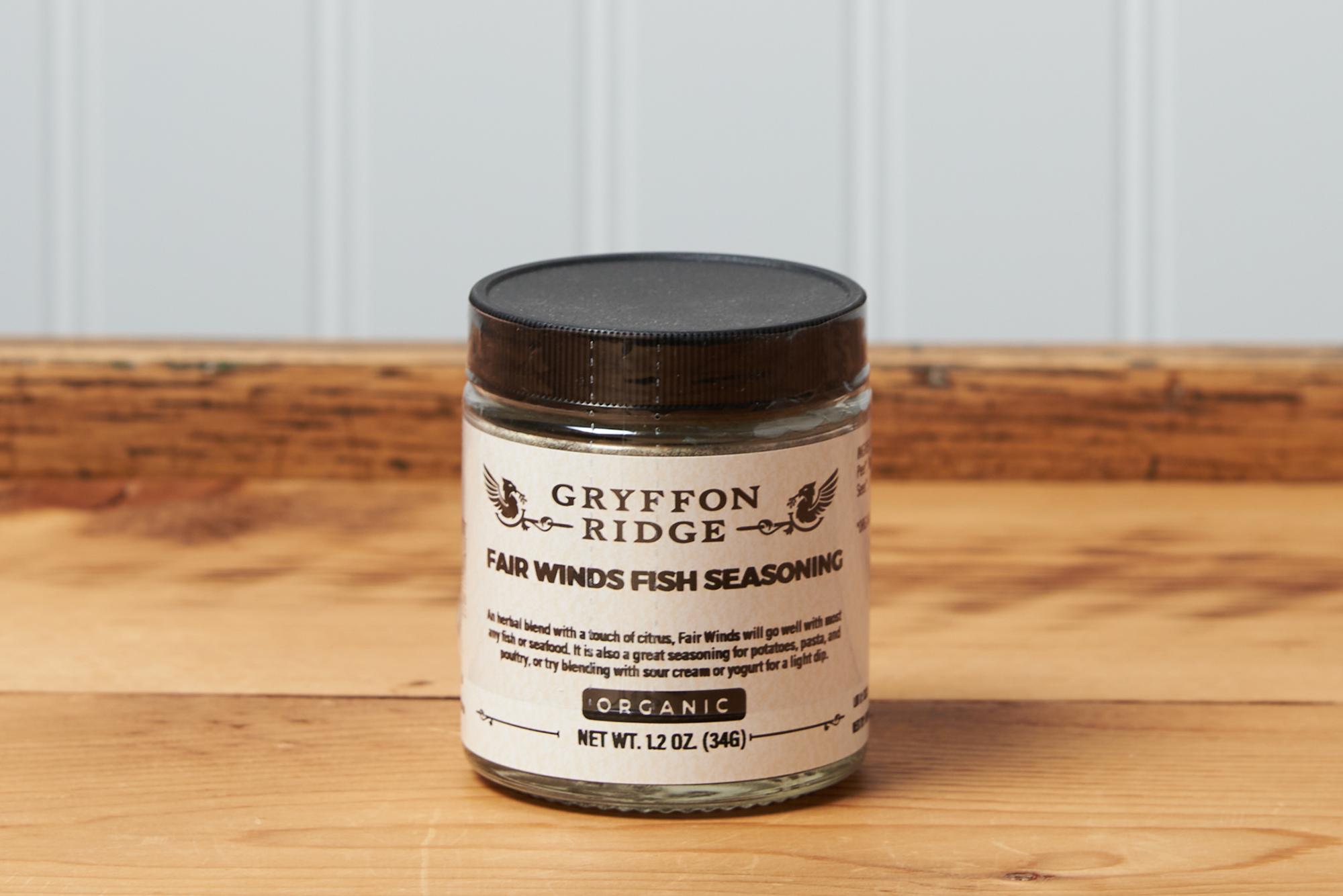 A jar of Gryffon Ridge Fair Winds Fish Seasoning sits on a wooden tabletop.