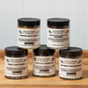 Five jars of Gryffon Ridge spices sit on a wooden tabletop. The spices include Casco Bay Seasoning, Fair Winds Fish Seasoning, Sumac Berry Powder, Turmeric Root Powder, and Senor Pistole’s Mild Chili Seasoning.