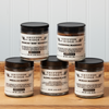 Five jars of Gryffon Ridge spices sit on a wooden tabletop. The spices include Aleppo Pepper Flakes, Blackening Seasoning, Jamaican “Jerk” Seasoning, Vindaloo Masala, and Sichuan Seasoning.