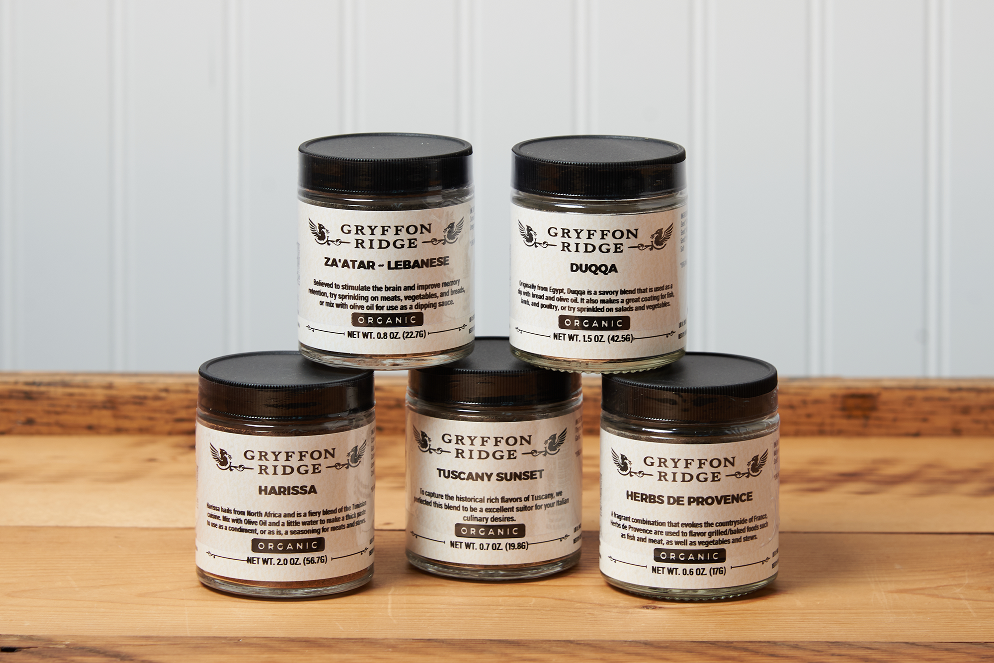 Five jars of Gryffon Ridge spices sit on a wooden tabletop. The spices include Tuscany Sunset, Harissa, Herbes de Provence, Lebanese Za’atar, and Duqqa