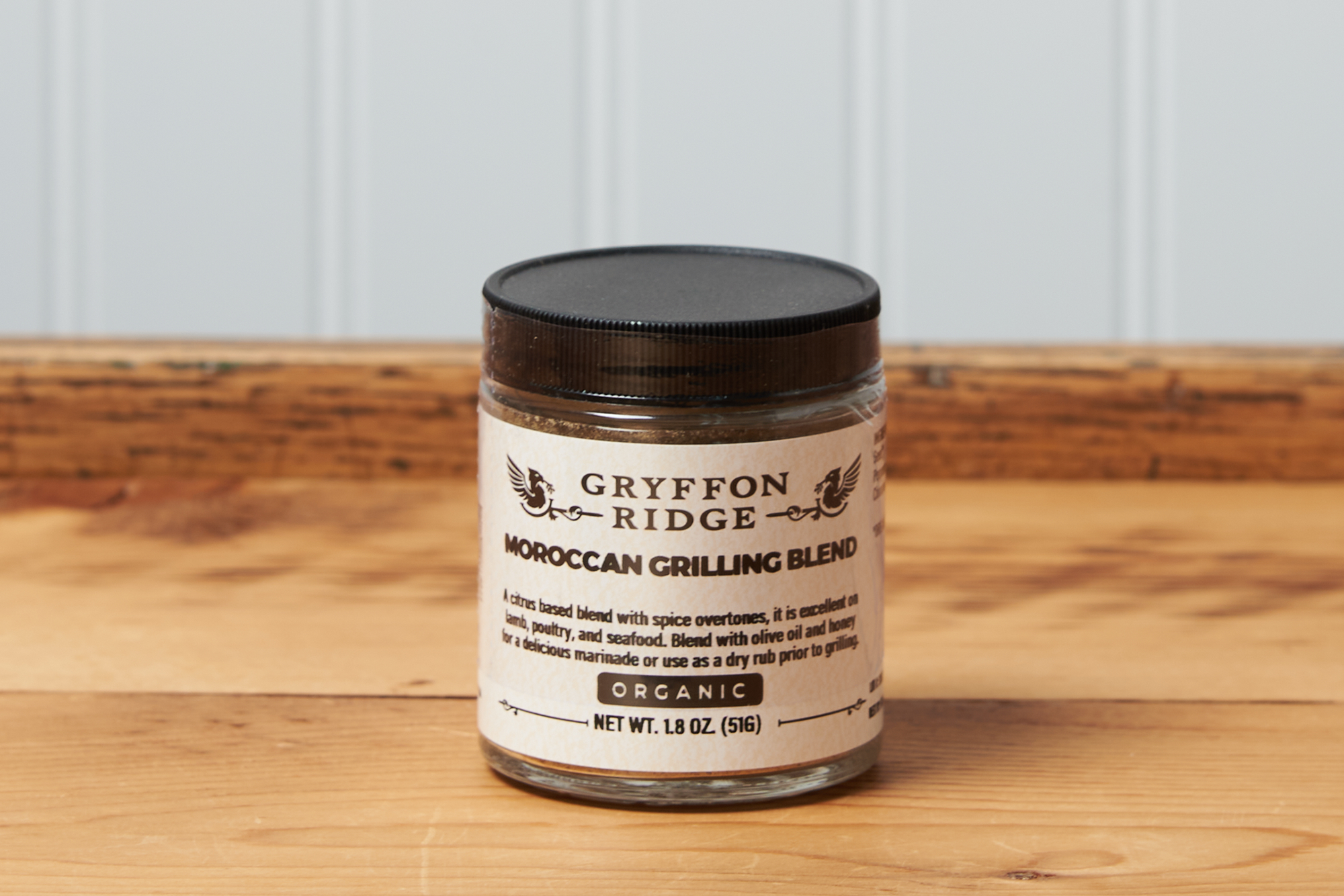 A jar of Gryffon Ridge Moroccan Grilling Blend sits on a wooden tabletop.