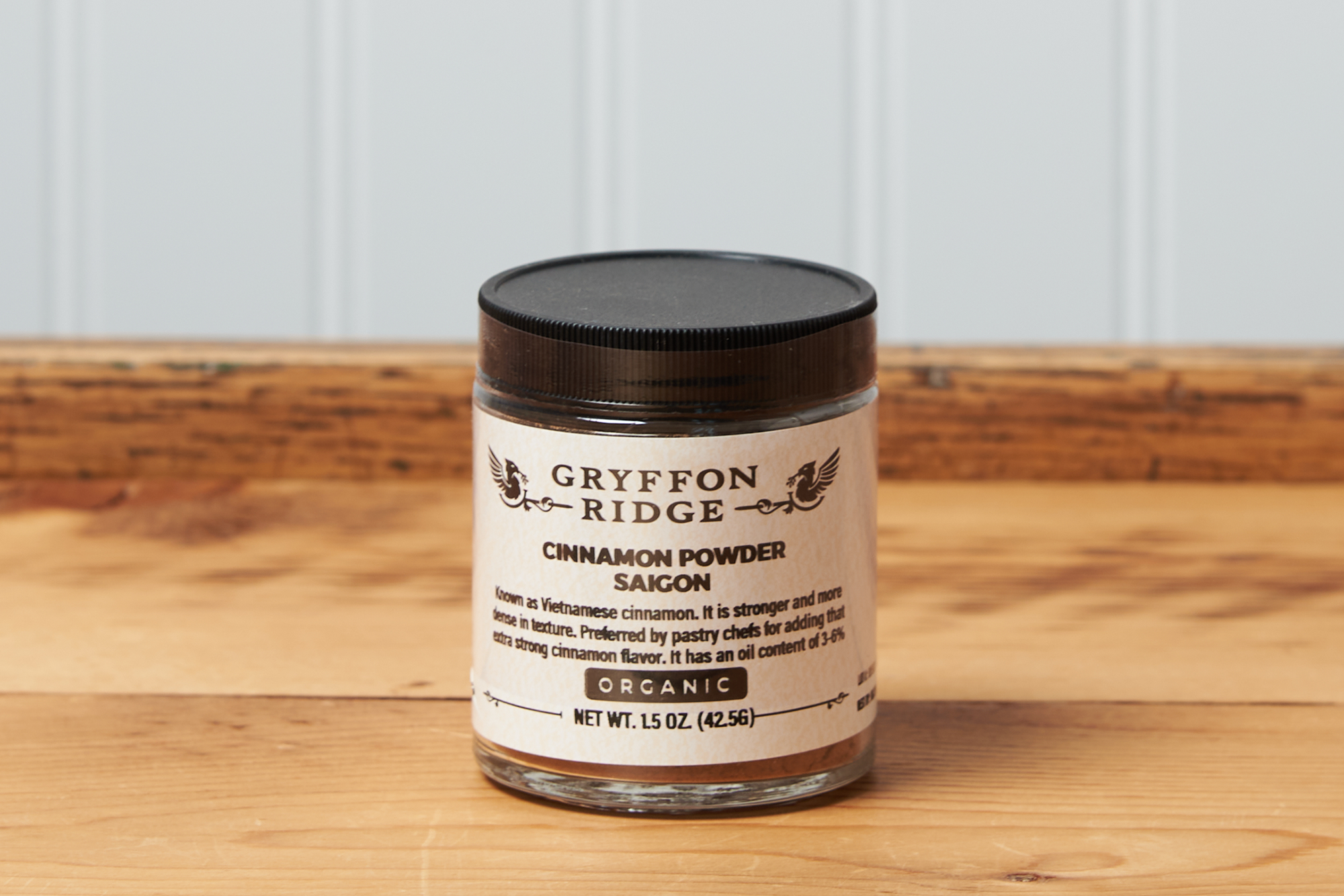 A jar of Gryffon Ridge Saigon Cinnamon Powder sits on a wooden tabletop.
