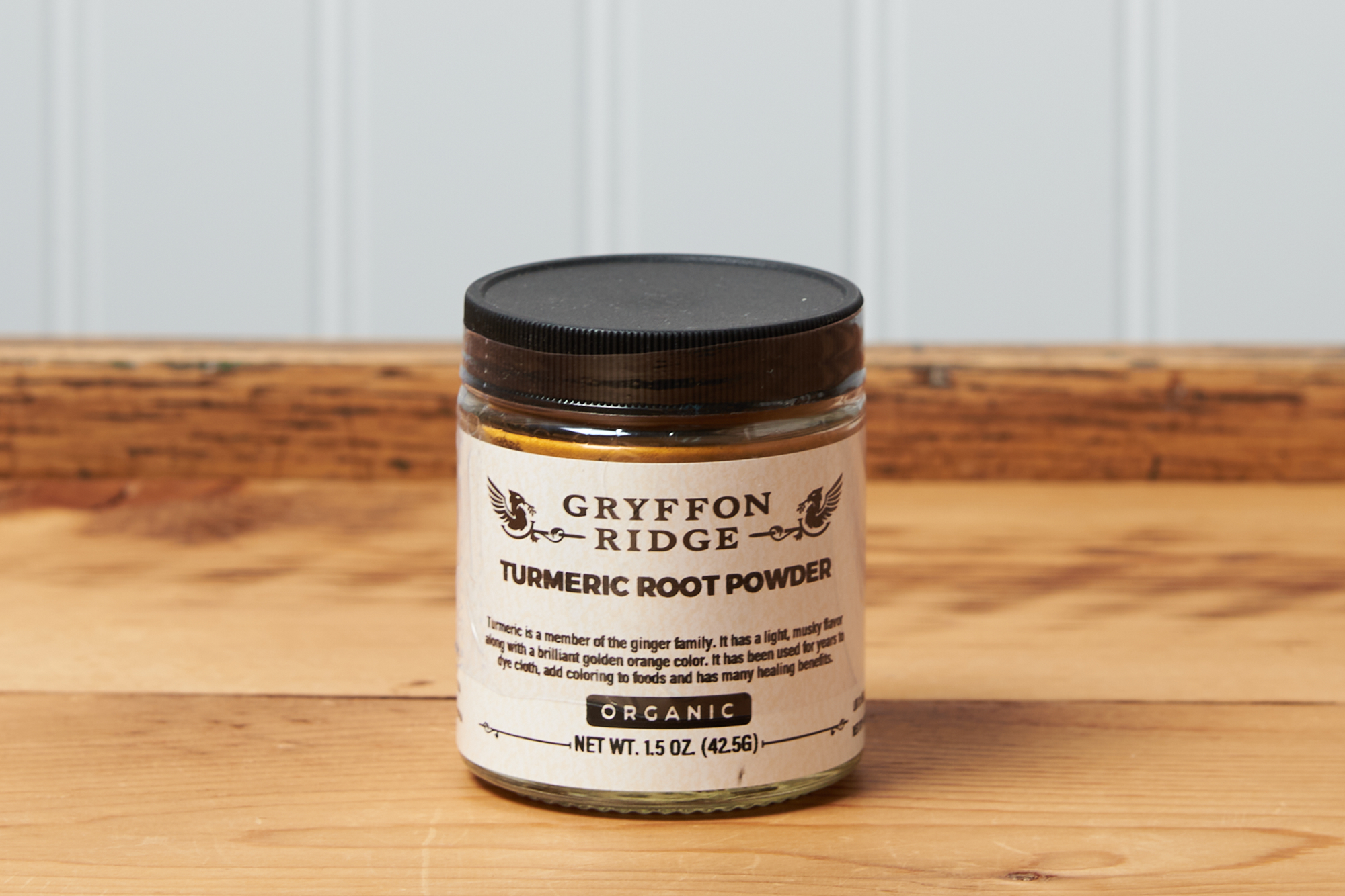 A jar of Gryffon Ridge Turmeric Root Powder sits on a wooden tabletop.
