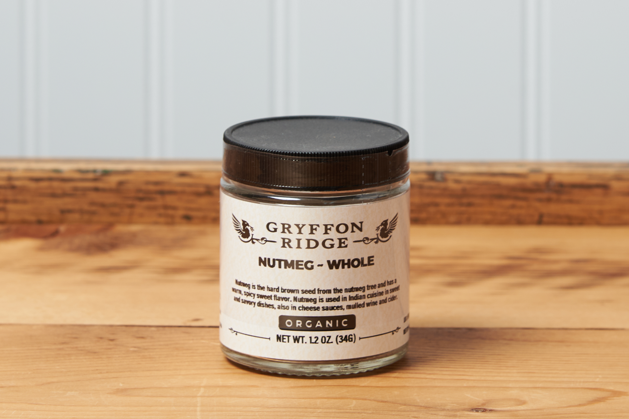 A jar of Gryffon Ridge Whole Nutmeg sits on a wooden tabletop.