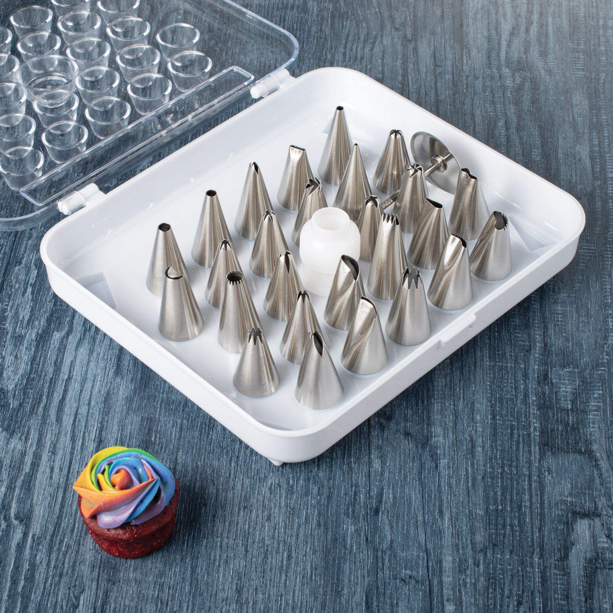 Mrs. Anderson's Baking Pastry Decorating Set, 26 Tips in a white case on a wooden surface with a small cake decorated with colorful frosting.