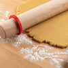 Rolling pin with a Mrs. Anderson's Baking Silicone Rolling Pin Ring on rolled-out dough on a wooden surface with flour.