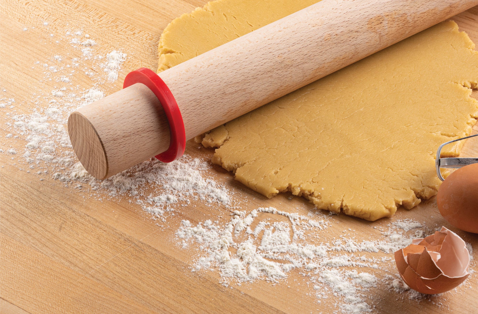 Rolling pin with a Mrs. Anderson's Baking Silicone Rolling Pin Ring on rolled-out dough on a wooden surface with flour.