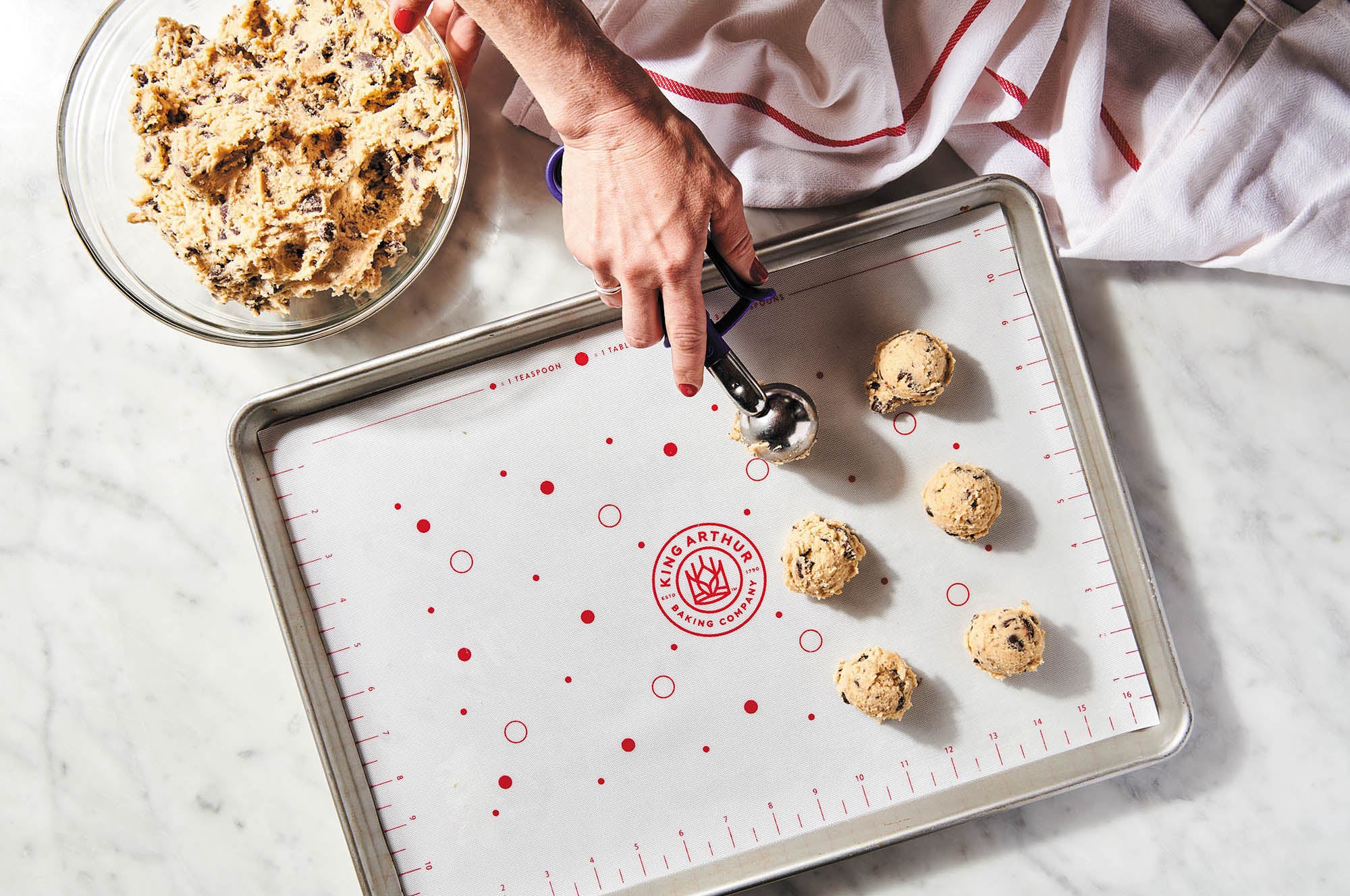Person scooping cookie dough onto a King Arthur Baking Company Cookie Mat.