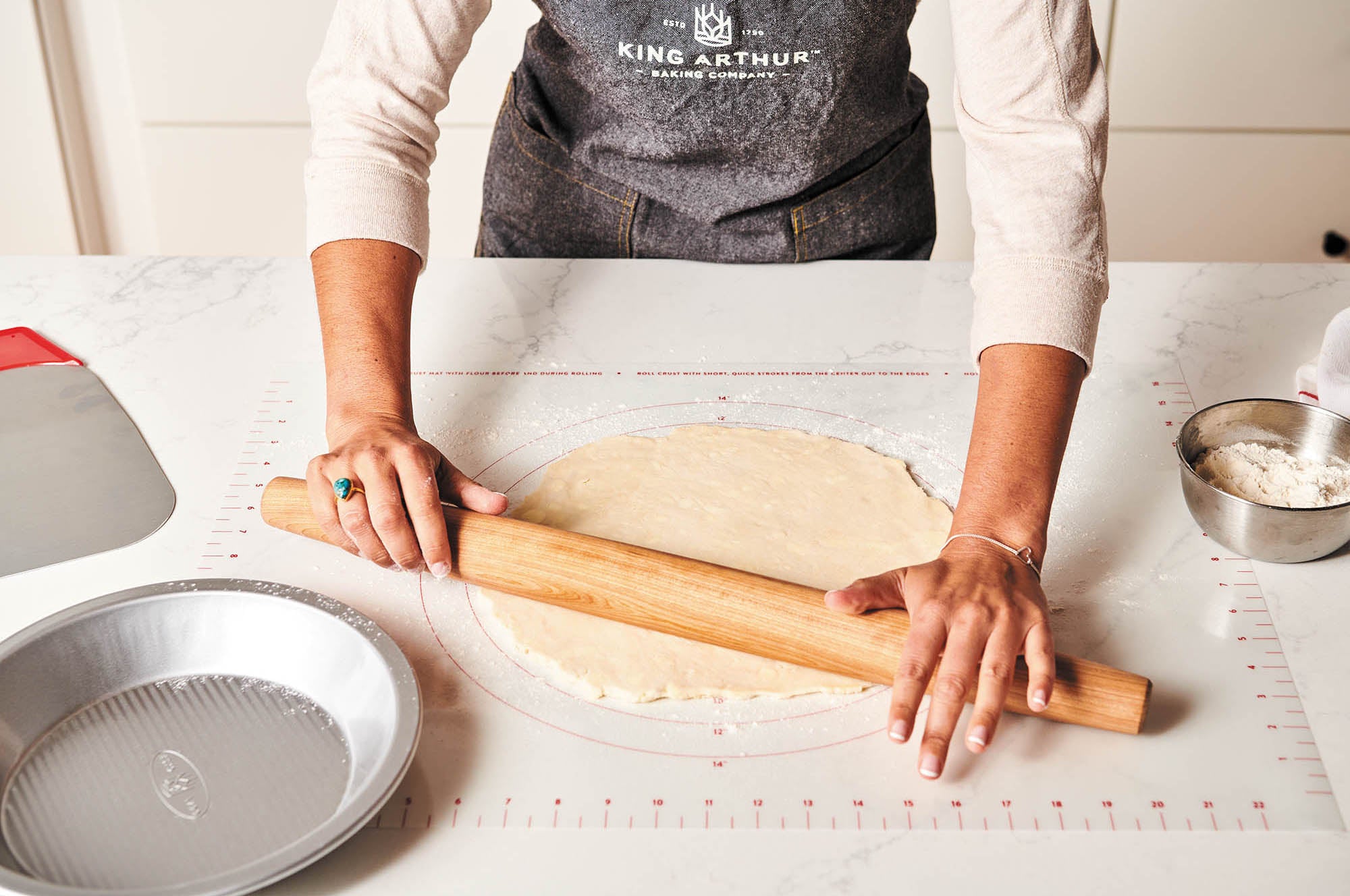 Person rolling out dough with a wooden rolling pin on a King Arthur Baking Company Rolling Mat.