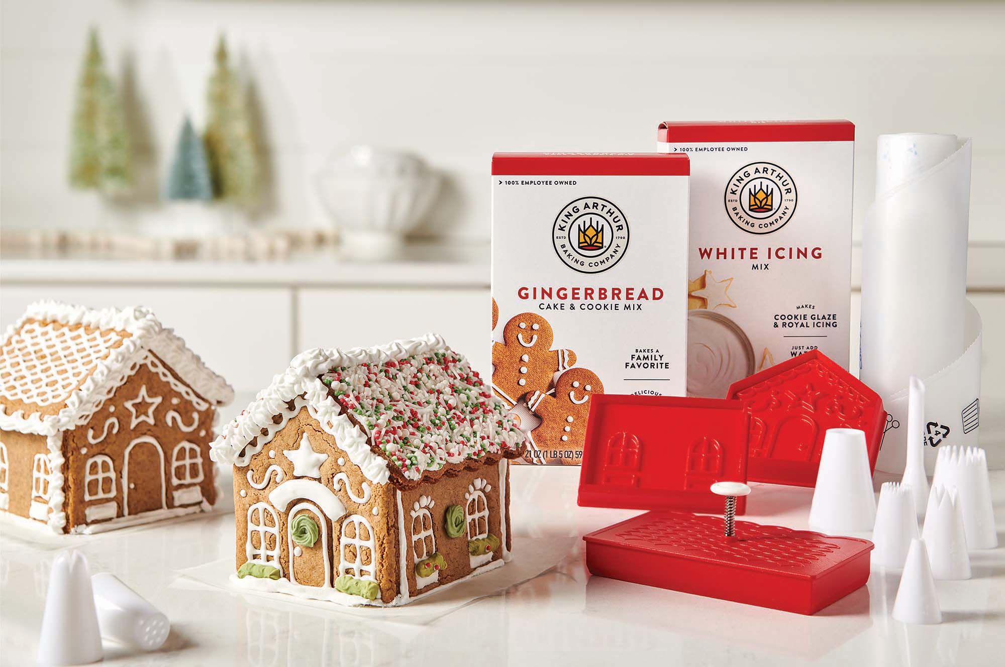 A King Arthur Baking Company 3-D Gingerbread Cutter Set sits alongside two completed gingerbread houses and boxes of baking mix on a white countertop.
