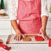 A person in a red apron uses the King Arthur Baking Company 3-D Gingerbread Cutter Set to make gingerbread houses in a kitchen.