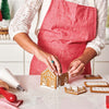 A person in a red apron uses the King Arthur Baking Company 3-D Gingerbread Cutter Set to make gingerbread houses in a kitchen.