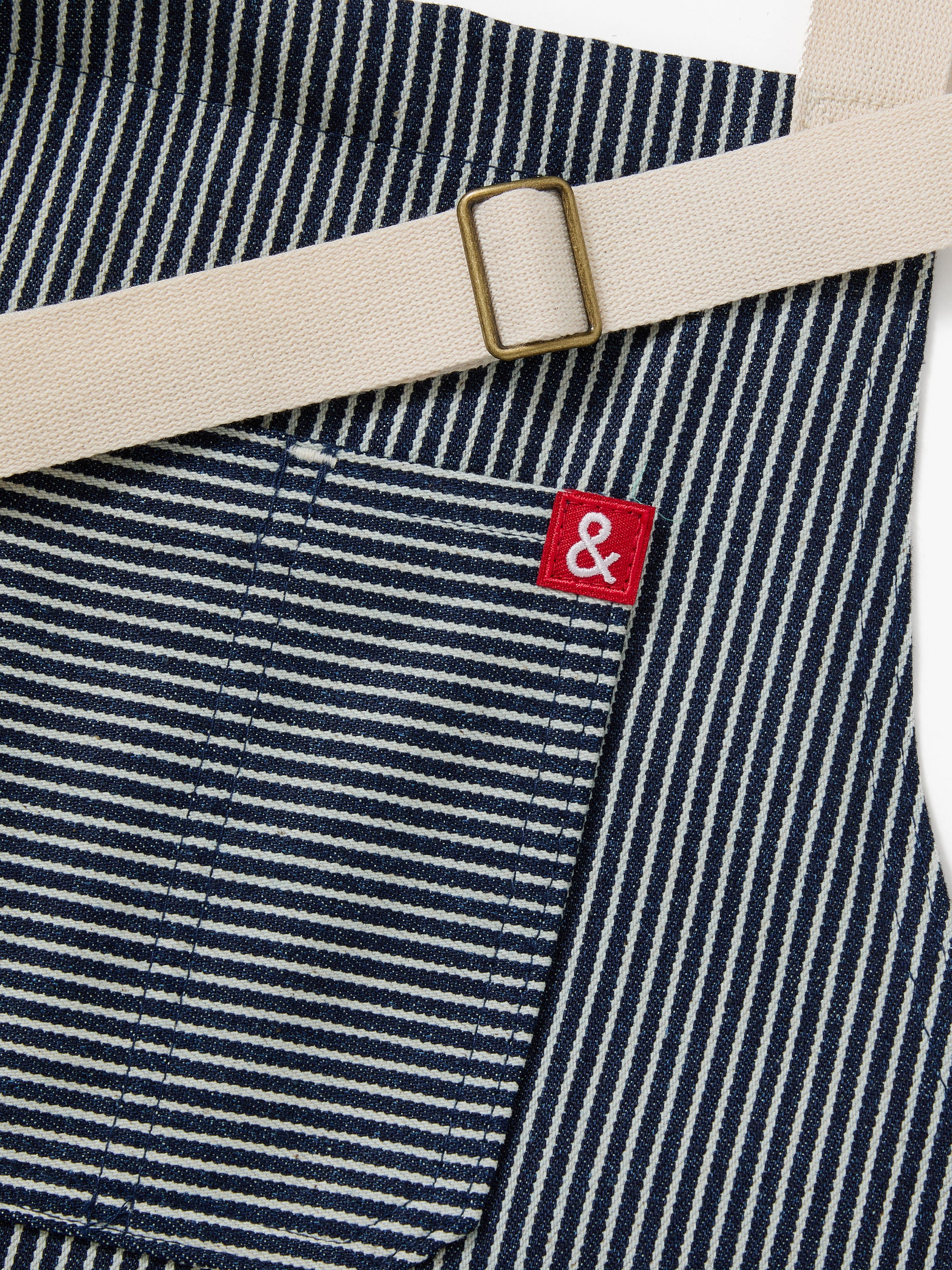 A close up shot of a Hedley & Bennett Hickory Stripe Essential Apron over a white background.