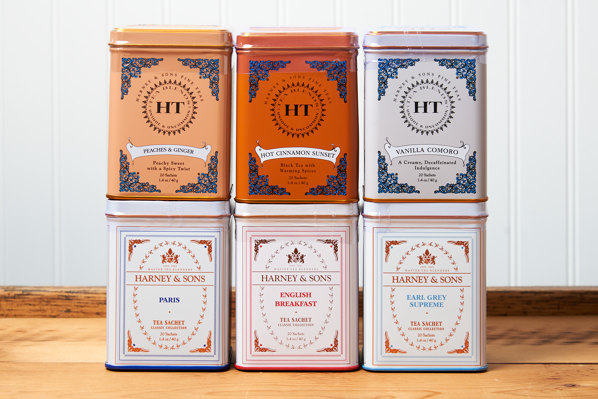 An assortment of Harney & Sons tea sits on a wooden countertop. The assortment includes the following teas: Hot Cinnamon Sunset, Paris, Vanilla Comoro, Earl Grey Supreme, English Breakfast, and Peaches and Ginger