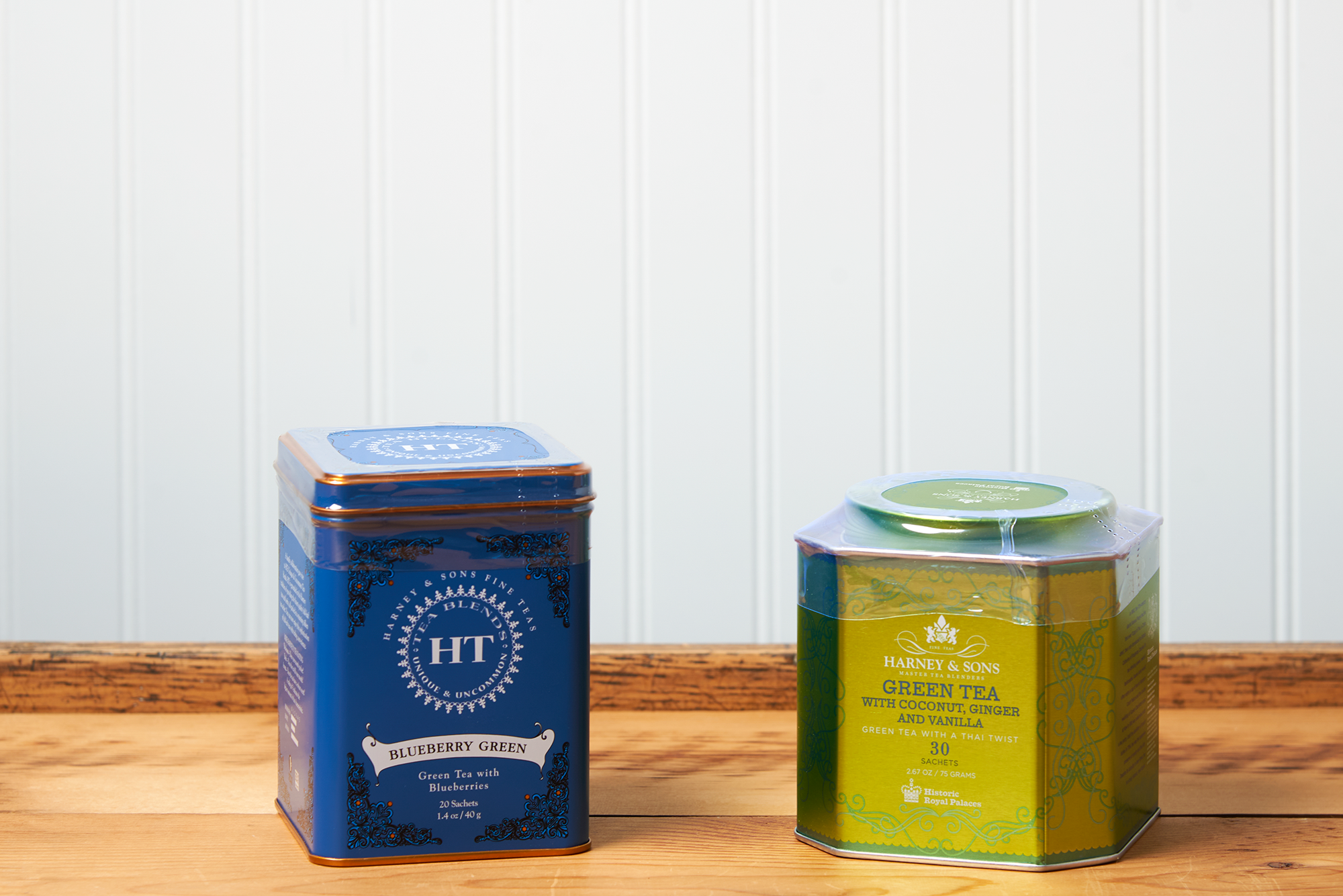 An assortment of Harney & Sons tea sits on a wooden countertop. The assortment includes the following teas: Blueberry Green and Green Tea with Coconut.