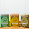 An assortment of Harney & Sons tea sits on a wooden countertop. The assortment includes the following teas: Ginger Lemon, Peppermint Herbal, and Ginger Turmeric.