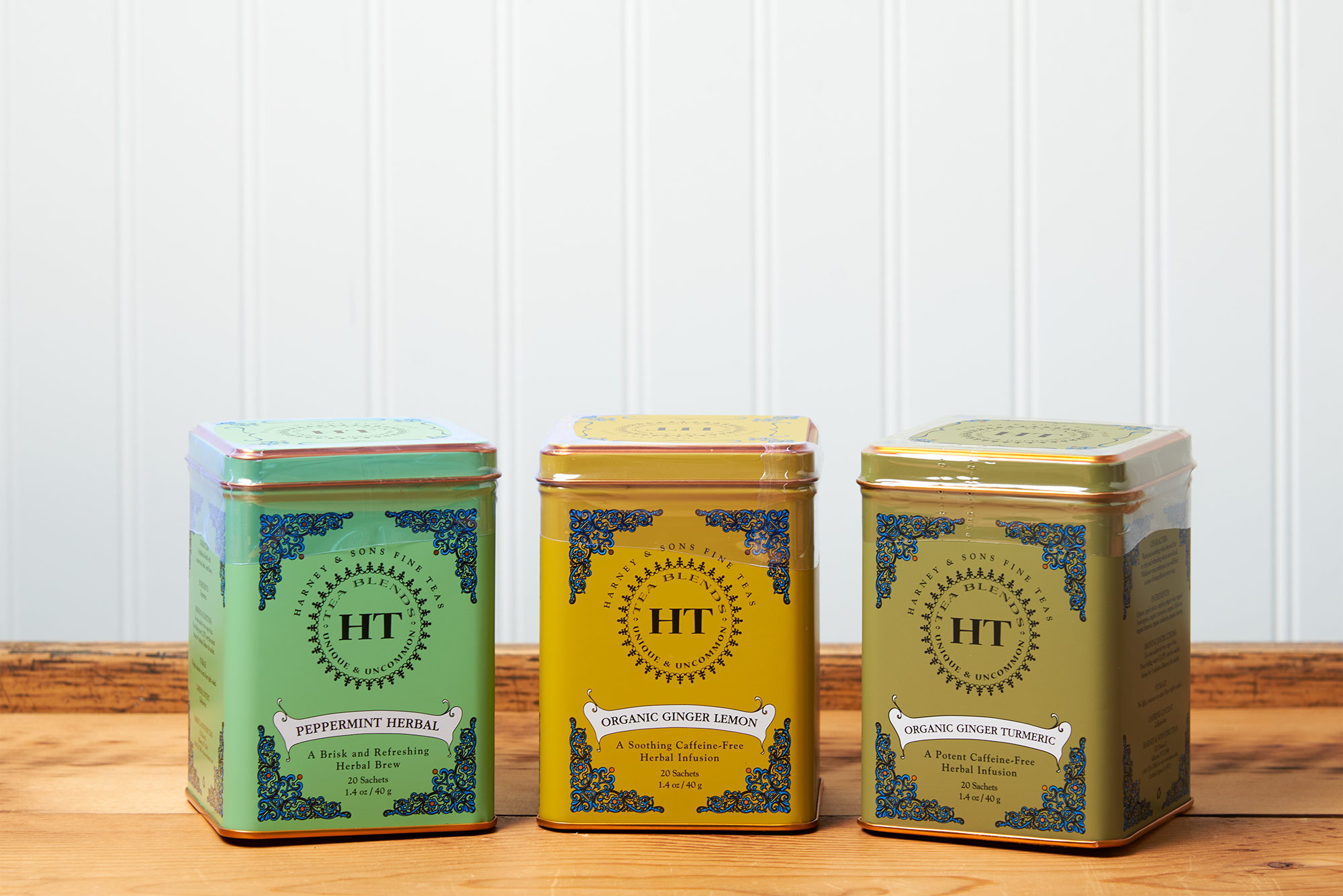 An assortment of Harney & Sons tea sits on a wooden countertop. The assortment includes the following teas: Ginger Lemon, Peppermint Herbal, and Ginger Turmeric.