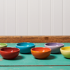 Six Le Creuset pinch bowls in assorted colors sit on a turquoise table.