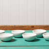 Six white Le Creuset pinch bowls in sit on a turquoise table.