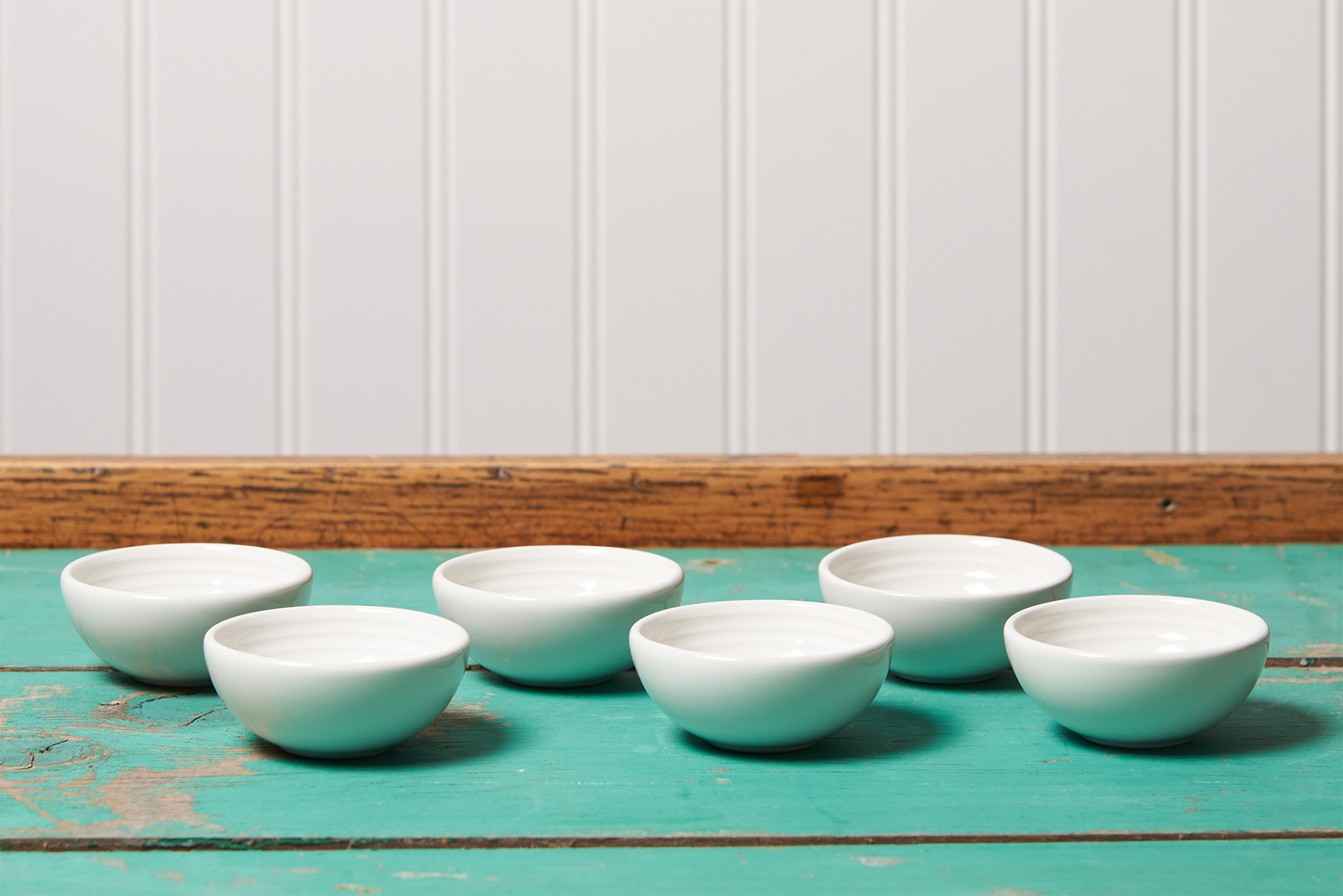 Six white Le Creuset pinch bowls in sit on a turquoise table.