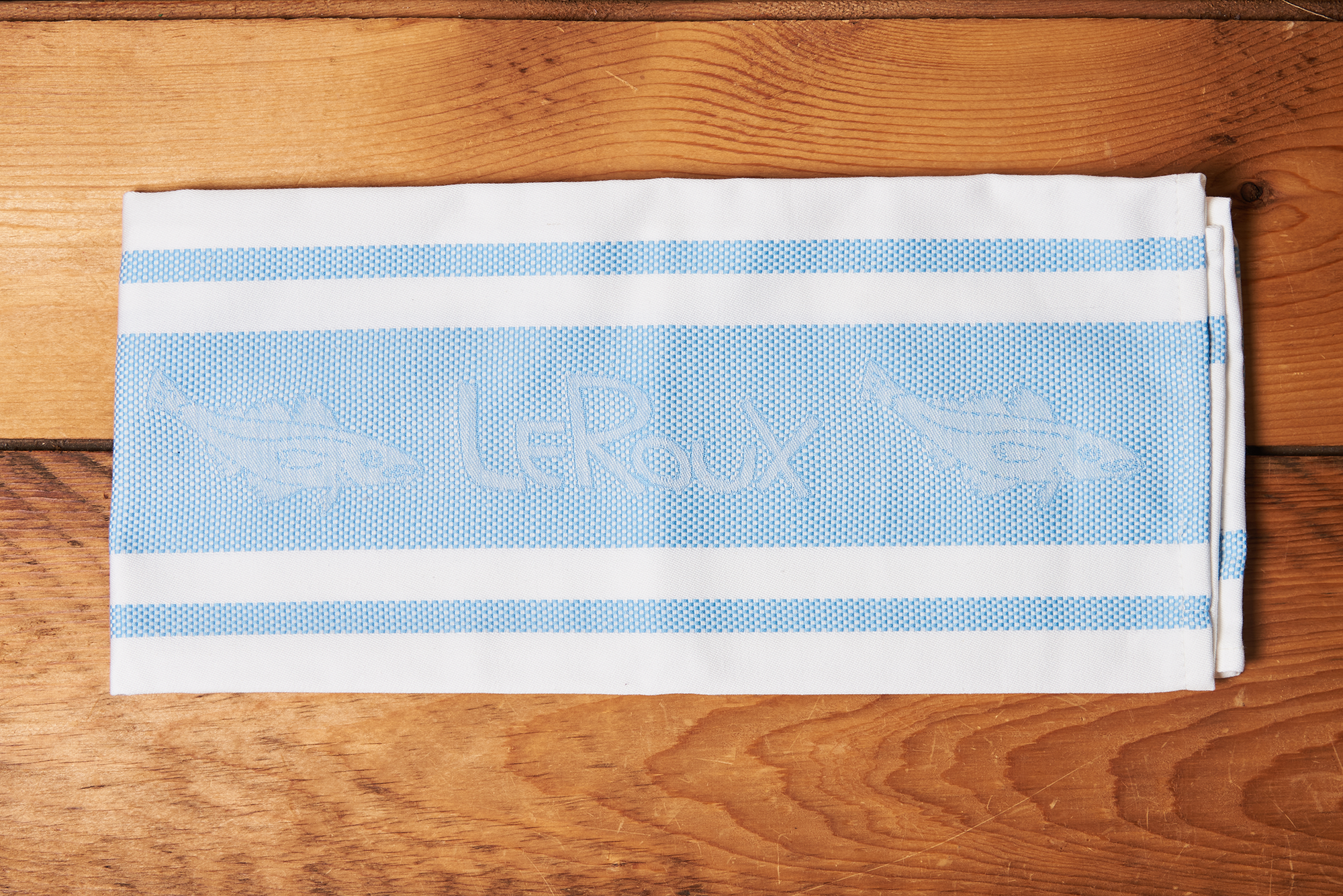 A blue LeRoux Jacquard Towel on a brown wooden table.