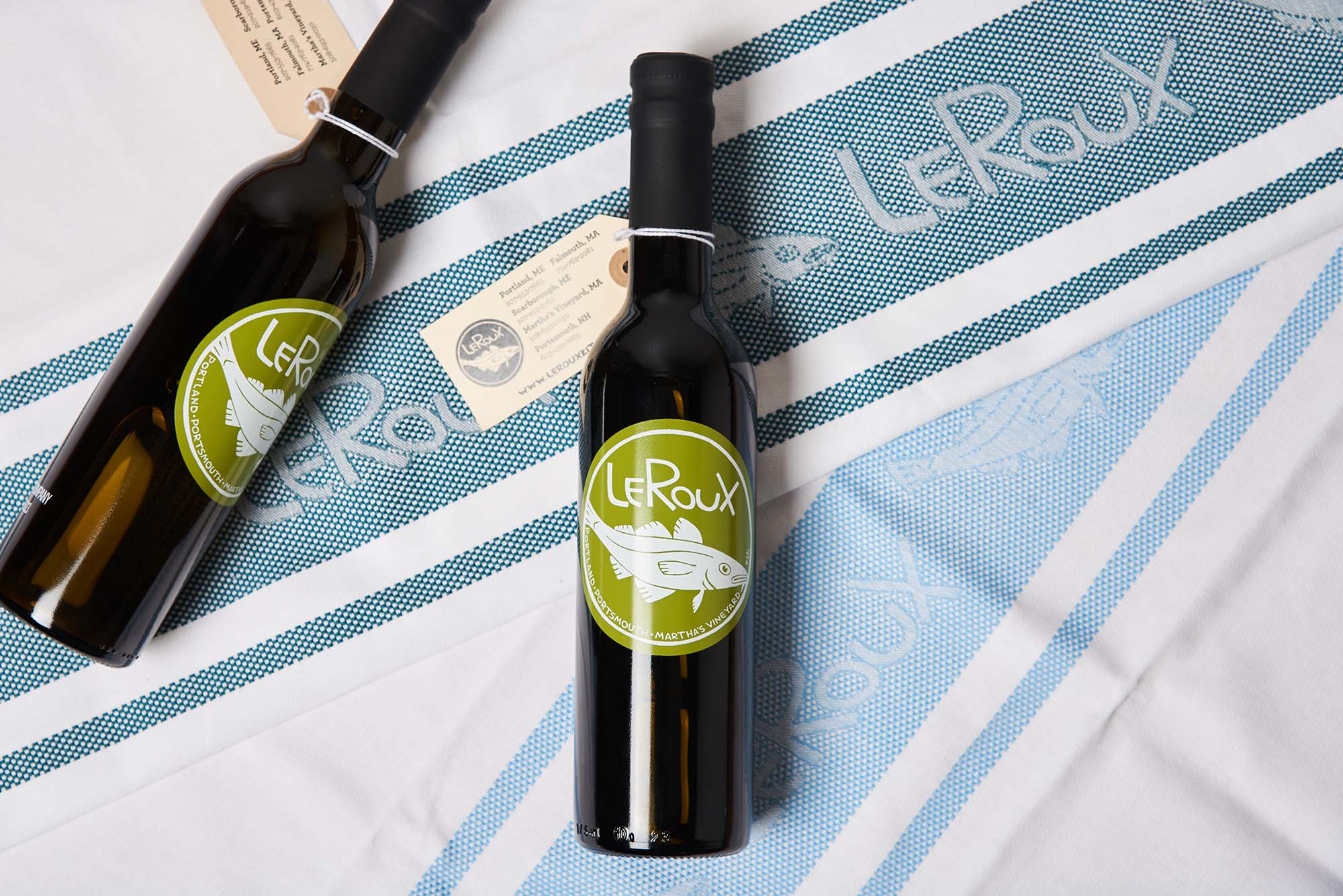 Two LeRoux Jacquard Towels lay underneath two bottles of olive oil and balsamic vinegar.