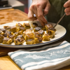 A man plates food. Alongside the plate, a LeRoux Jacquard Towel sits on the countertop.