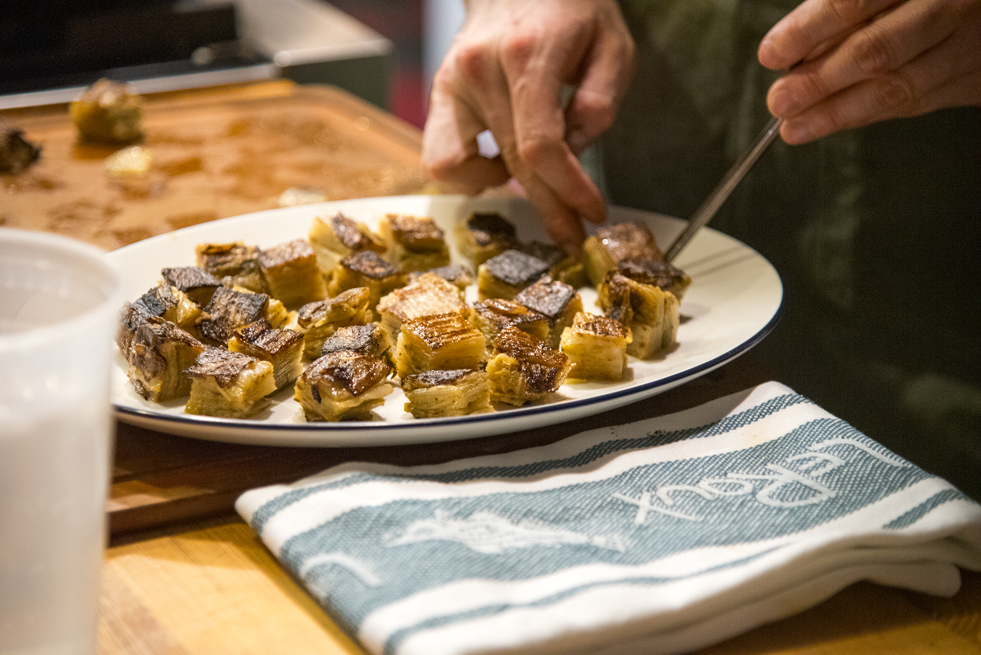 A man plates food. Alongside the plate, a LeRoux Jacquard Towel sits on the countertop.