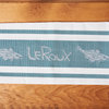 A teal LeRoux Jacquard Towel on a brown wooden table.