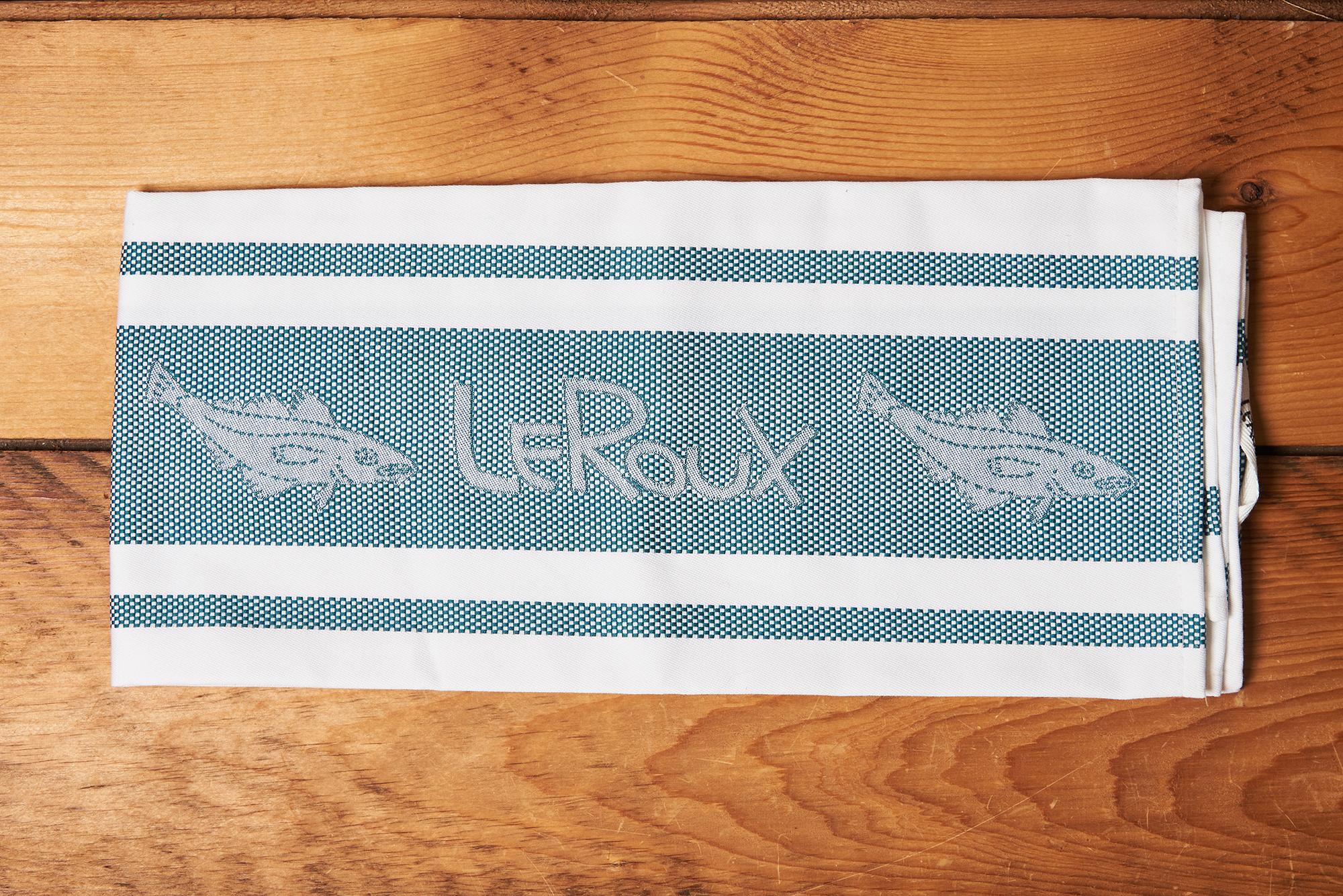 A teal LeRoux Jacquard Towel on a brown wooden table.
