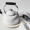 A Le Creuset Classic Kettle in White sits on a marble countertop alongside a kitchen towel.