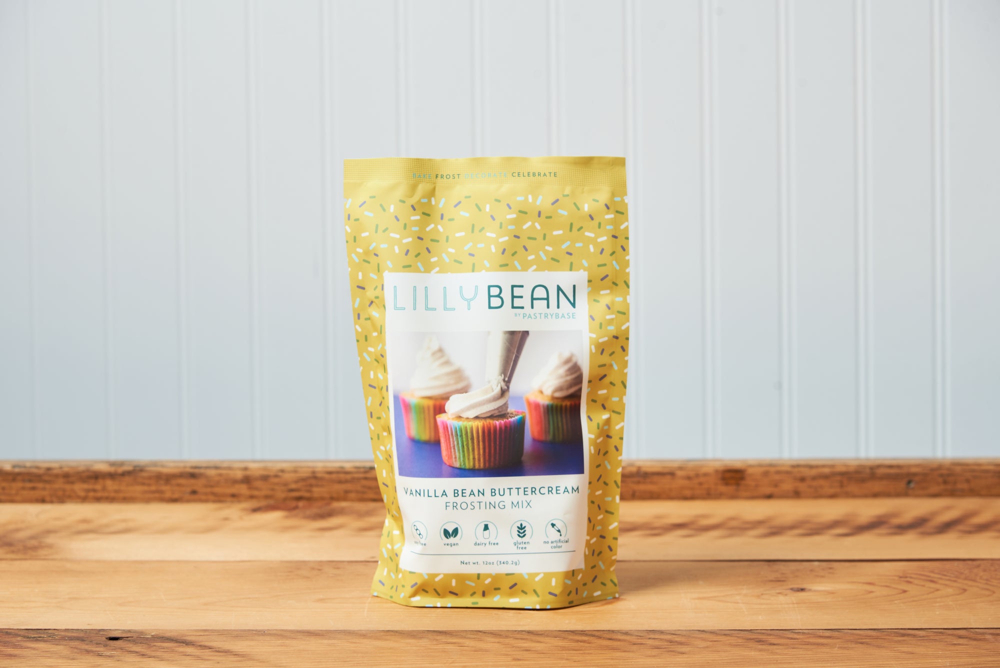 A bag of LillyBean Vanilla Bean Buttercream Frosting Mix sits on a wooden tabletop. 