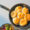 A Made In Carbon Steel Fry Pan sits on a countertop with seven biscuits.