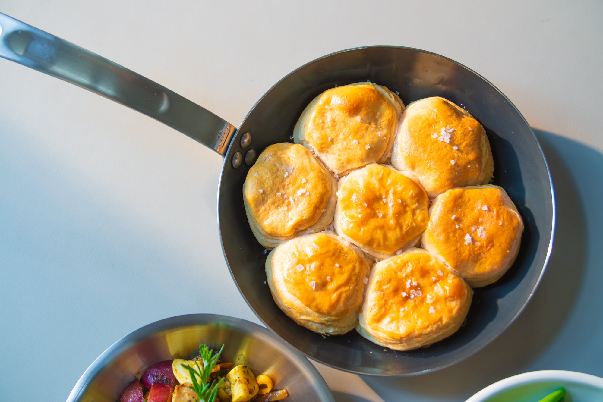A Made In Carbon Steel Fry Pan sits on a countertop with seven biscuits.